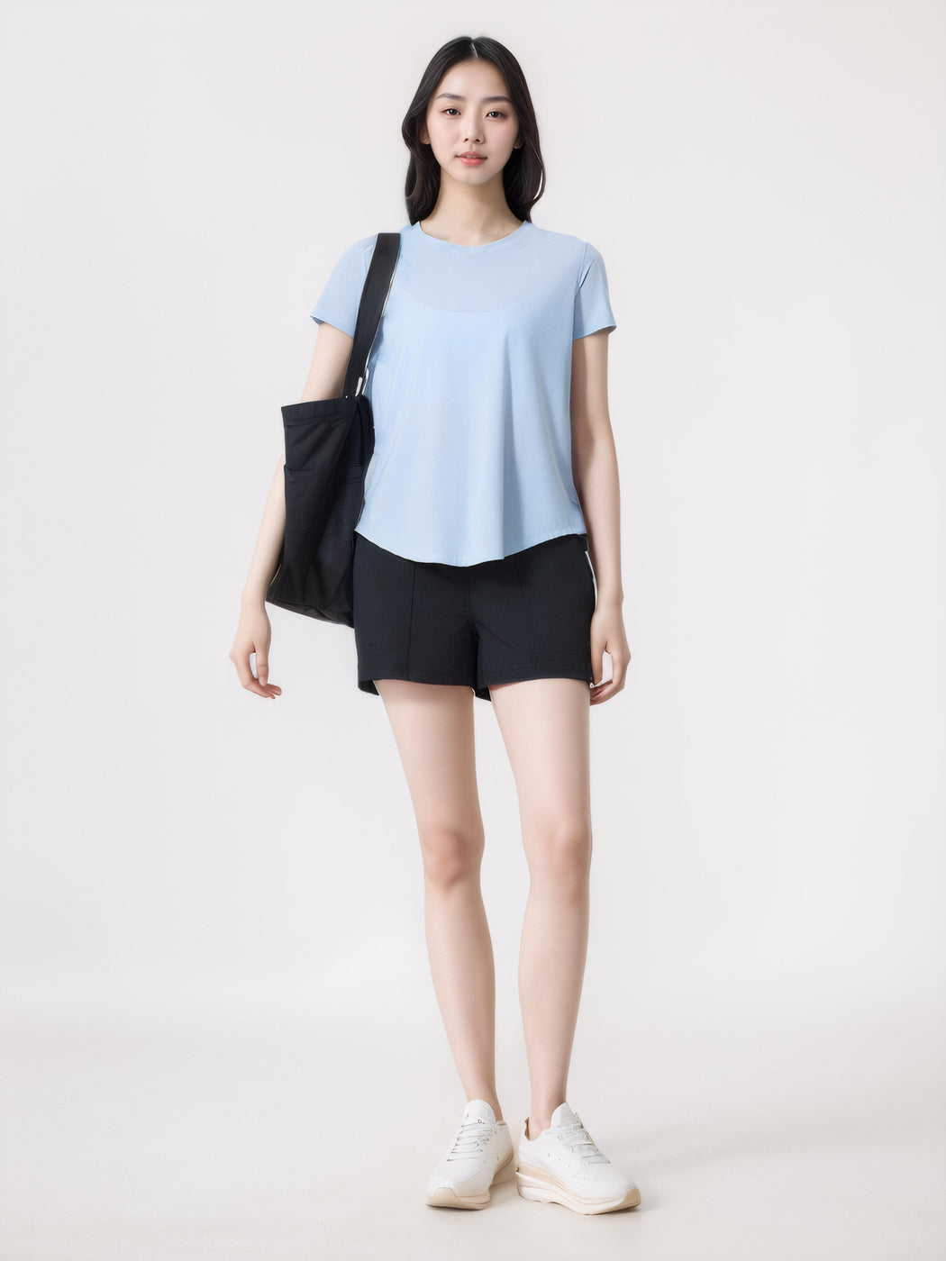 Woman wearing light blue Aero Flow Active Tee with black shorts and white sneakers, carrying black tote bag.