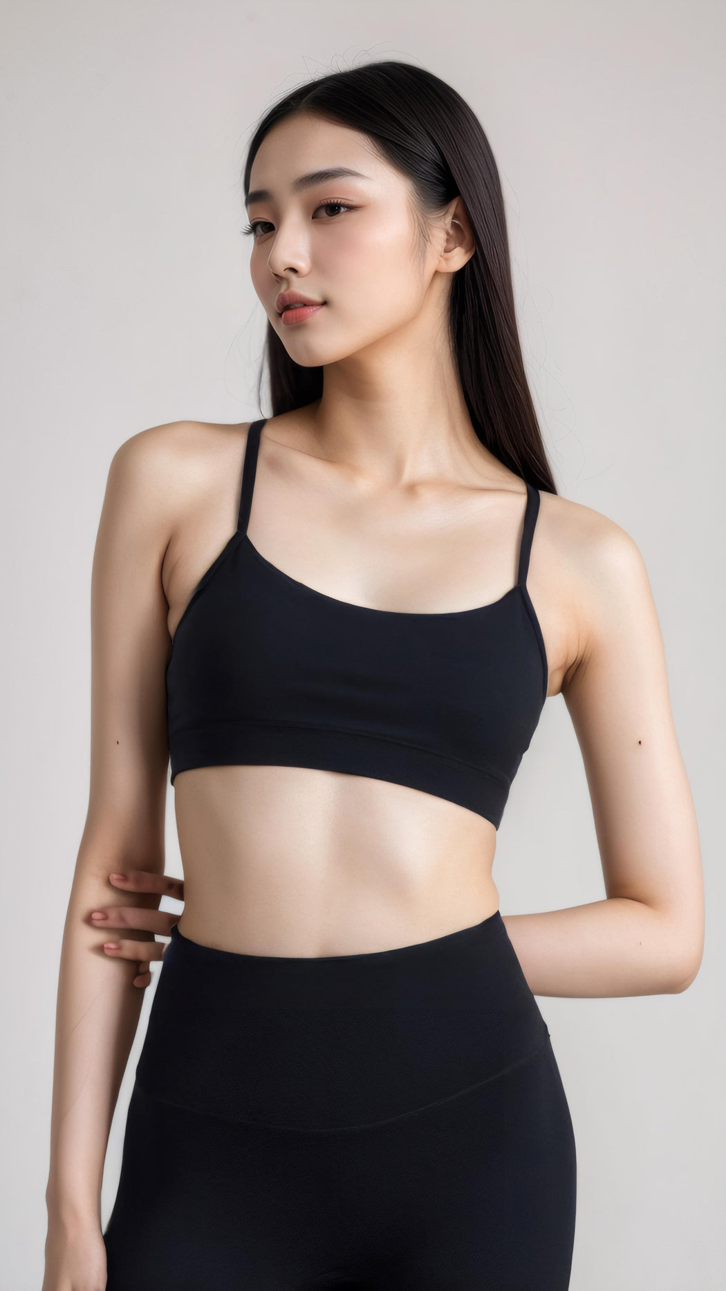 Woman wearing black AeroFlex Strappy Bra with thin straps and high-waisted black leggings, posing sideways.