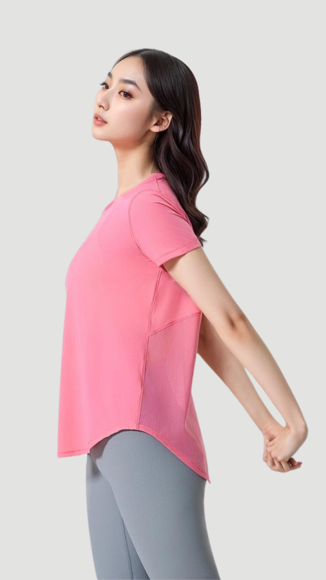 Woman stretching wearing a pink Aero Flow Active Tee with back slit and round neckline, paired with gray leggings.