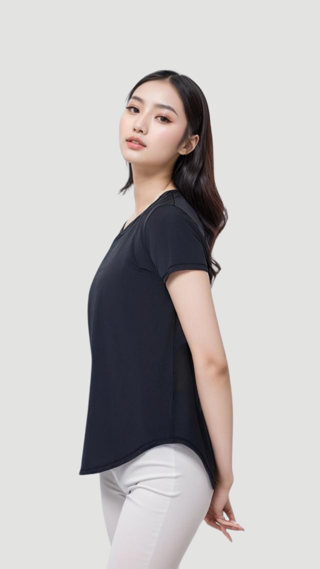 Woman wearing black Aero Flow Active Tee showing side profile with back slit and white pants against a plain background
