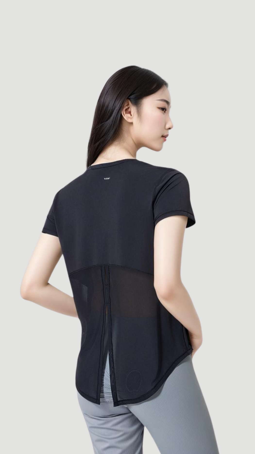 Woman wearing black Aero Flow Active Tee with back slit design and short sleeves, shown from behind on gray background.
